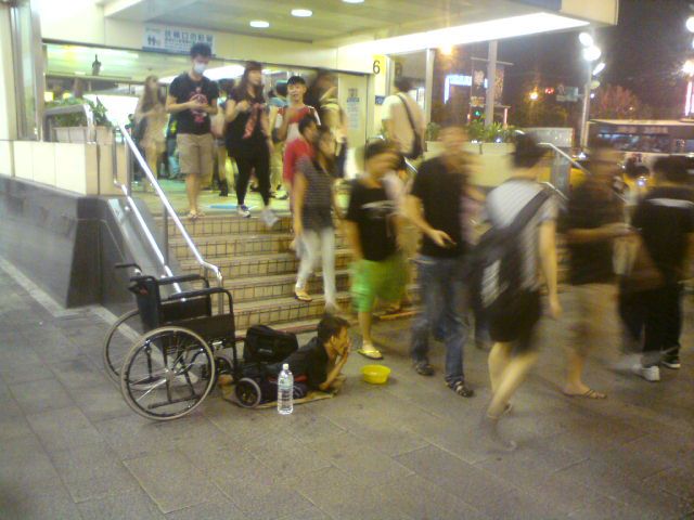 台北の若者街、西門町。　障害者はクルマ椅子から降りて地面に伏せながらハーモニカを演奏し聴衆からお金を乞うている。